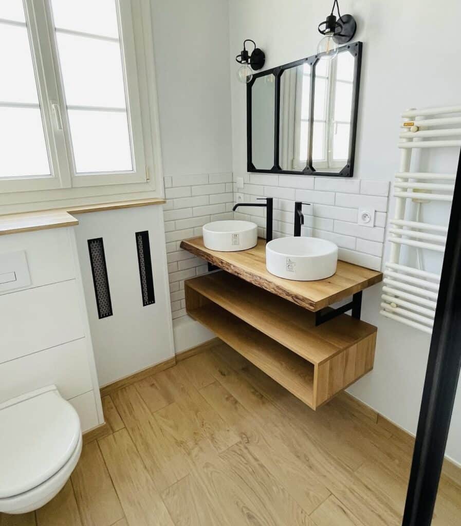 Salle de bain rénovée avec double vasque ronde sur plan bois massif, miroir cadre noir, carrelage métro blanc et sol imitation bois
