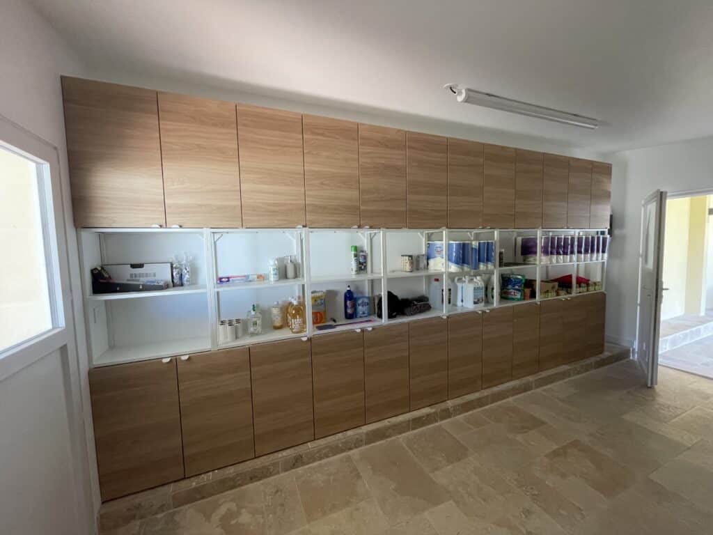 Grande buanderie avec rangement mural sur mesure en bois clair, étagères ouvertes et sol en travertin beige