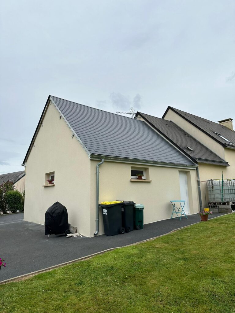 Maison rénovée avec façade enduite beige et toiture en ardoise neuve, allée en enrobé noir et pelouse verdoyante