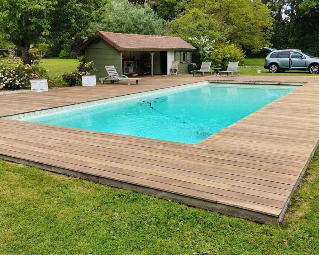 Piscine rectangulaire avec large terrasse en bois exotique IPE entourant l'ensemble du bassin, pool house vert en arrière-plan