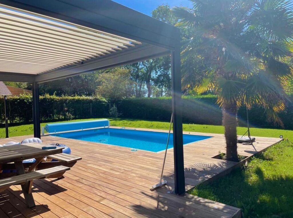 Piscine rectangulaire avec volet roulant, terrasse en bois exotique et pergola bioclimatique à lames orientables dans un jardin arboré
