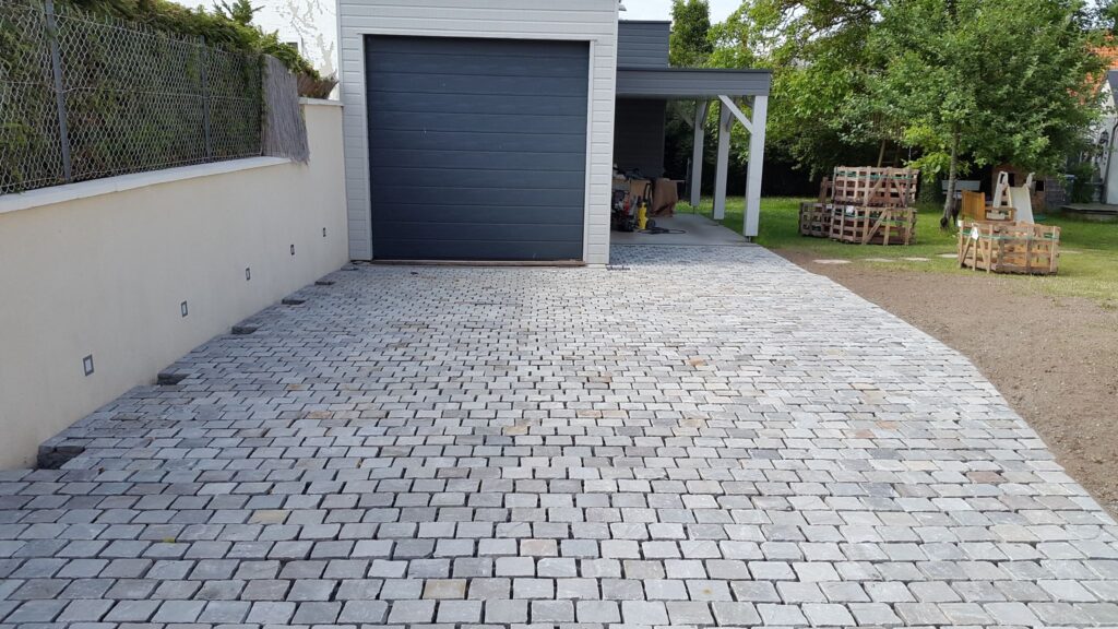 Allée de garage pavée en pavés granit gris anthracite devant un garage moderne à porte sectionnelle grise