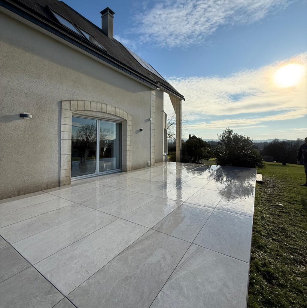 Terrasse en carrelage grand format gris poli devant une maison de style traditionnel avec vue dégagée sur la campagne