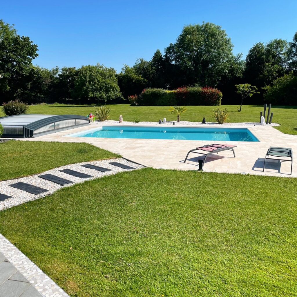 Piscine rectangulaire avec abri bas coulissant dans un jardin paysager avec pelouse et chaises longues