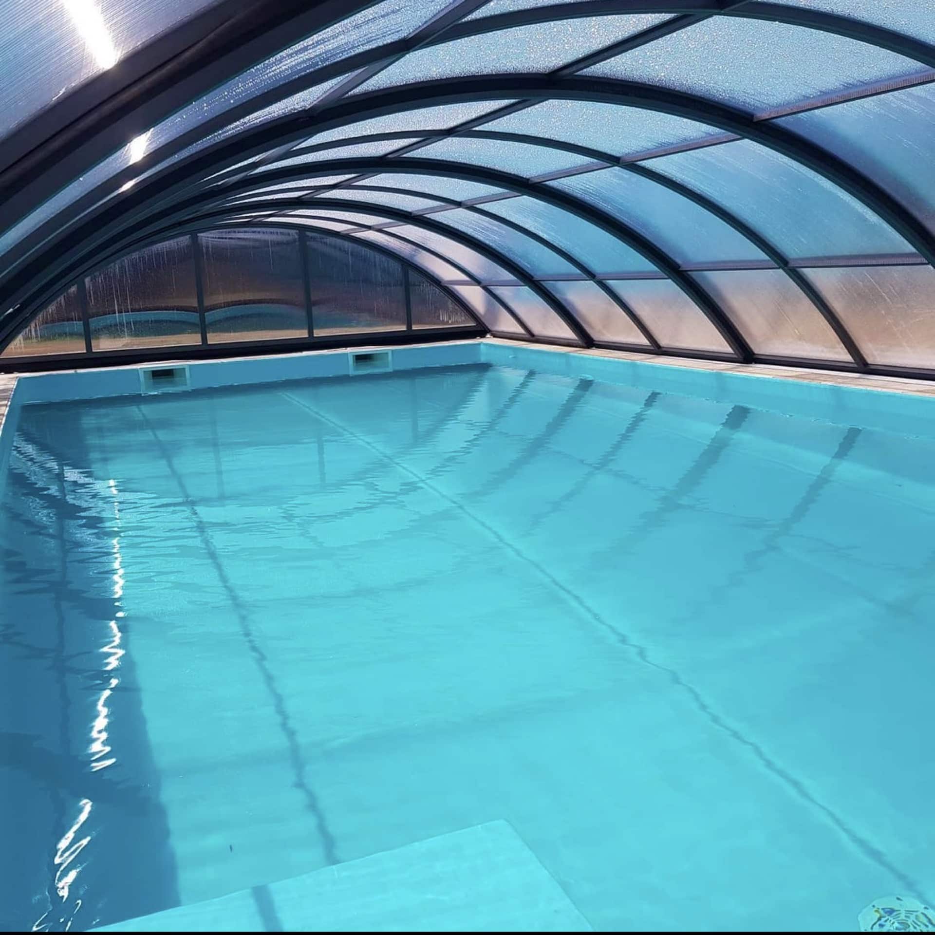 Piscine privée aux eaux turquoise protégée par un abri en polycarbonate transparent à structure métallique grise