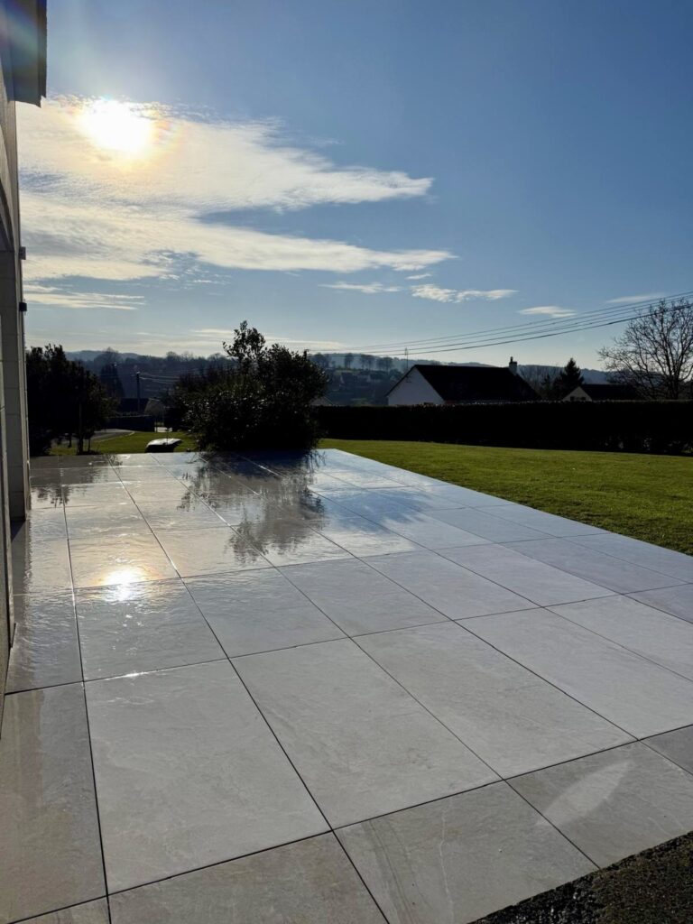 Grande terrasse en carrelage poli gris clair avec vue dégagée sur jardin - GL Travaux Calvados